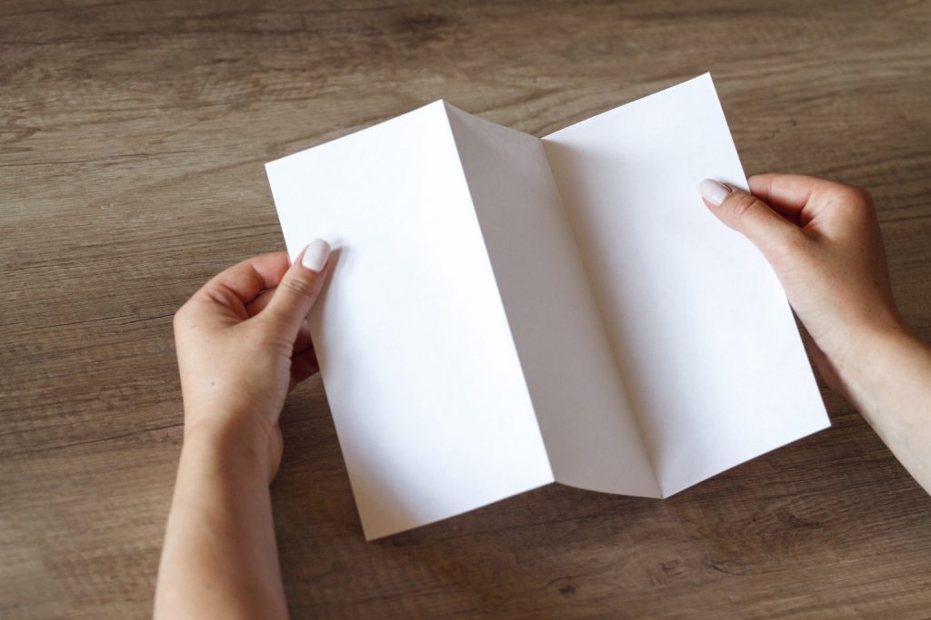 Hands folding a blank sheet of paper into a tri fold brochure
